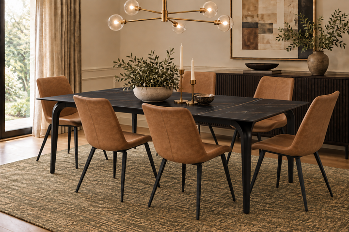 A modern dining room set featuring a rectangular black stone table with black metal legs and six upholstered chairs in a warm tan suede or velvet fabric with black legs, set on a textured beige rug.
